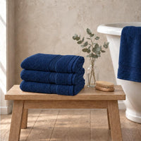 Set of three navy Egyptian cotton luxury bath sheets, 650gsm, stacked on an oak bench beside a roll-top bath